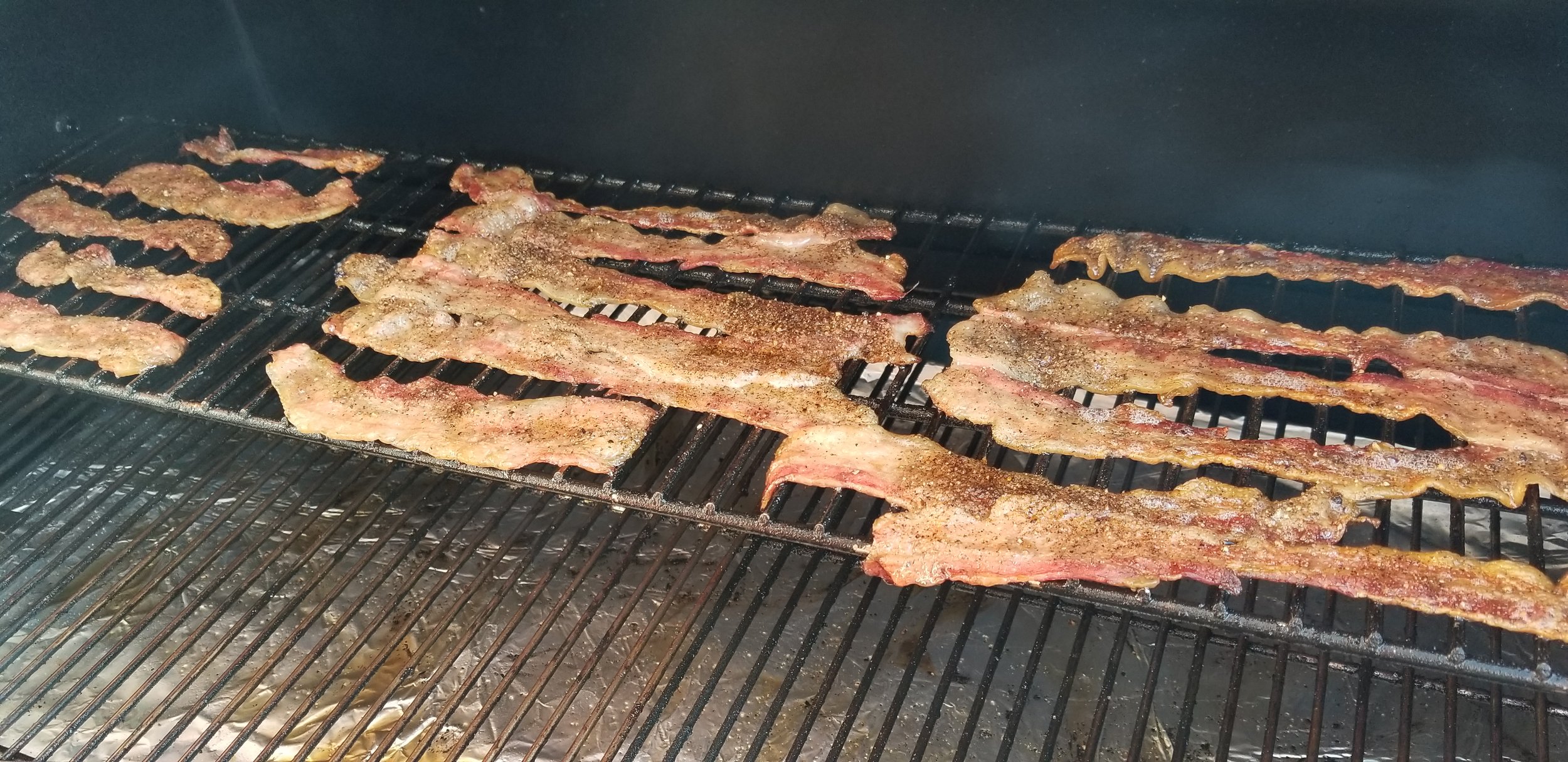 Bacon strips sizzling on a grill with a smoky background, showcasing a savory cooking process ideal for barbecue enthusiasts.