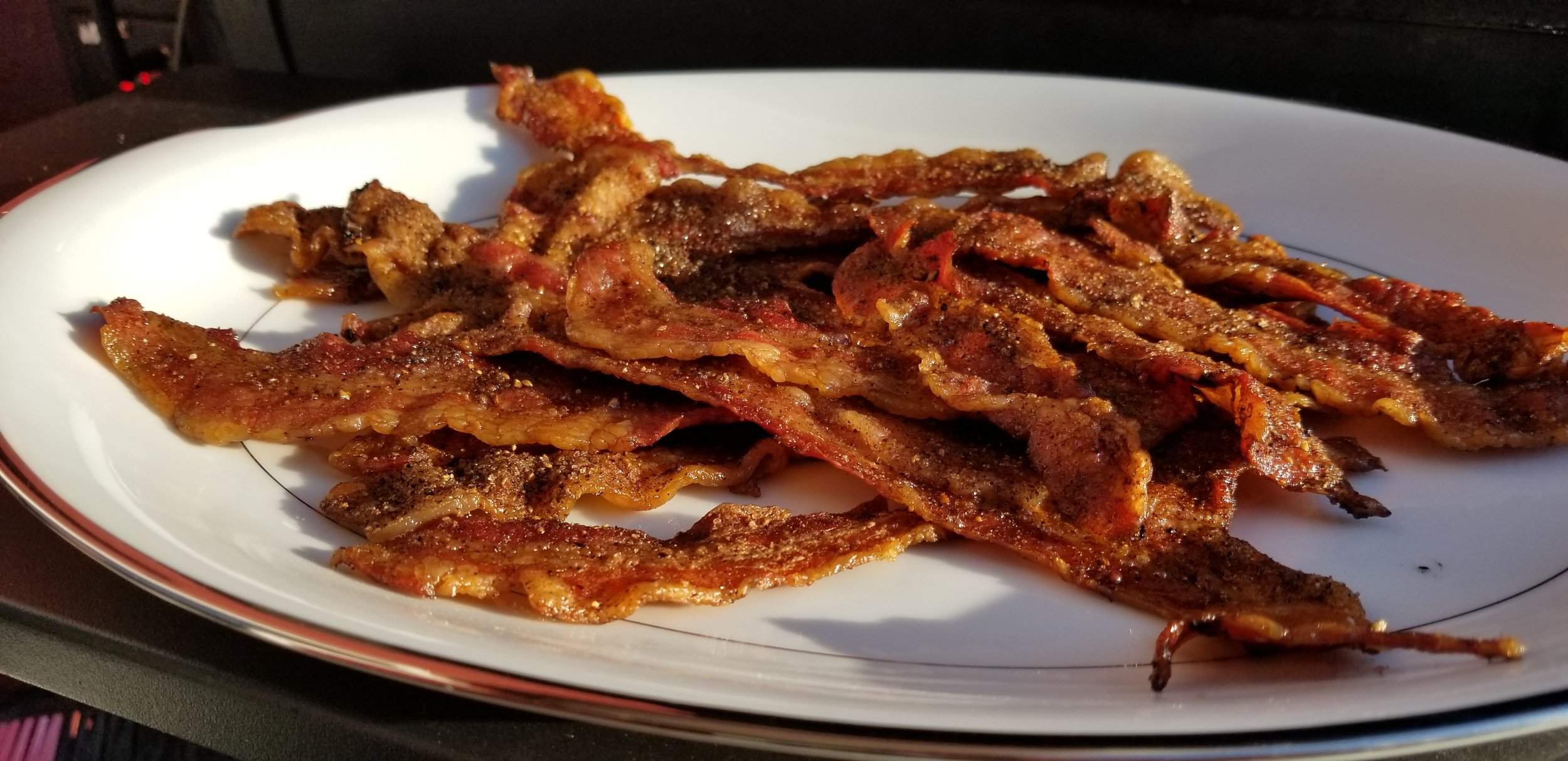 Crispy, golden-brown bacon strips arranged on a white plate, showcasing a deliciously seasoned texture perfect for breakfast or as a savory snack.