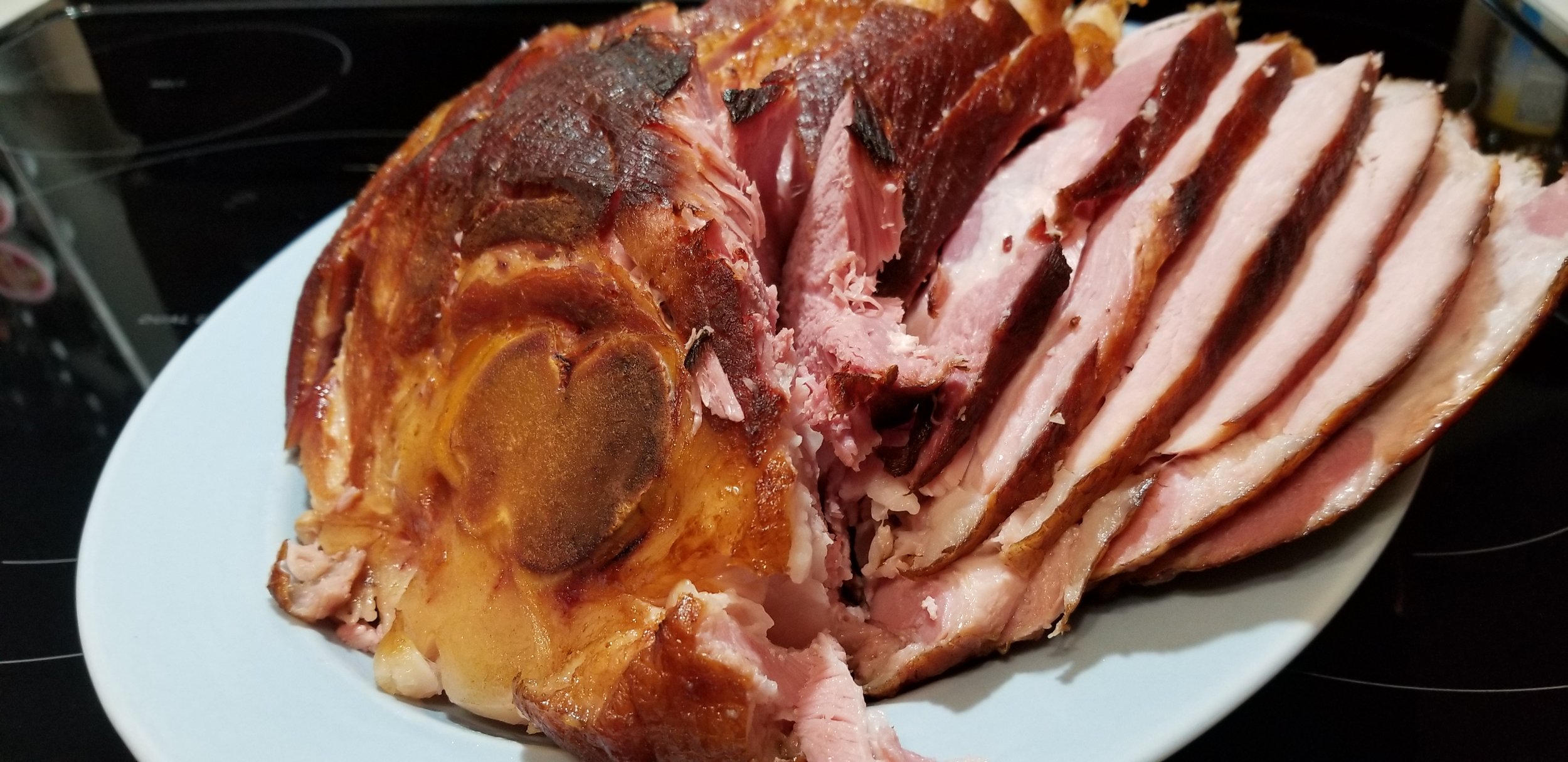 Sliced honey glazed ham on a white plate, showcasing juicy pink meat and crispy brown edges, perfect for holiday meals or family gatherings.