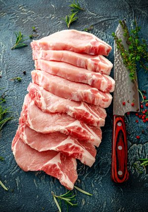 Freshly sliced pork chops arranged neatly on a textured surface, accompanied by a sharp kitchen knife and garnished with herbs. Ideal for recipes and cooking inspiration.
