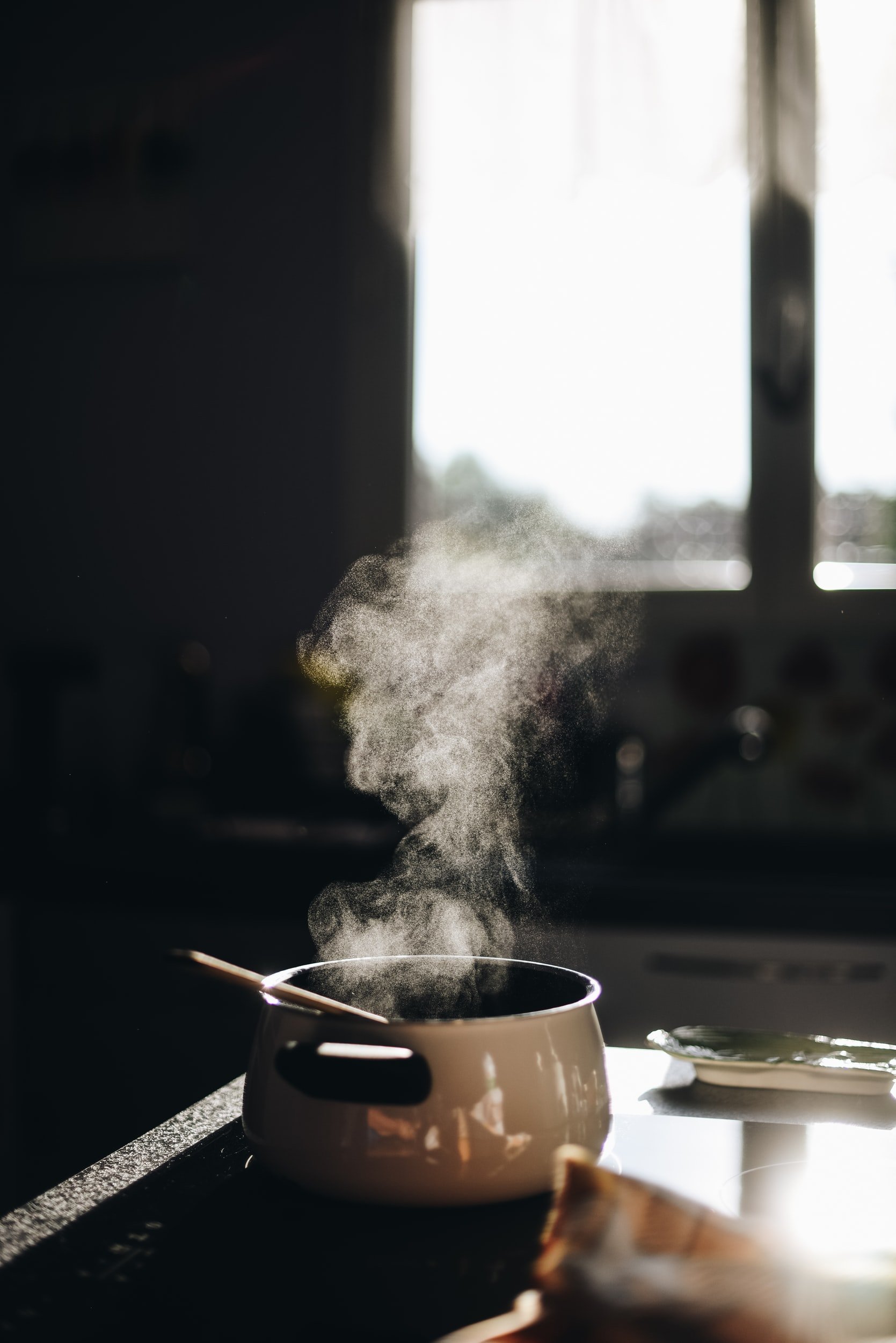 A cooking pot on a kitchen countertop with steam rising, illuminated by natural light from a nearby window.